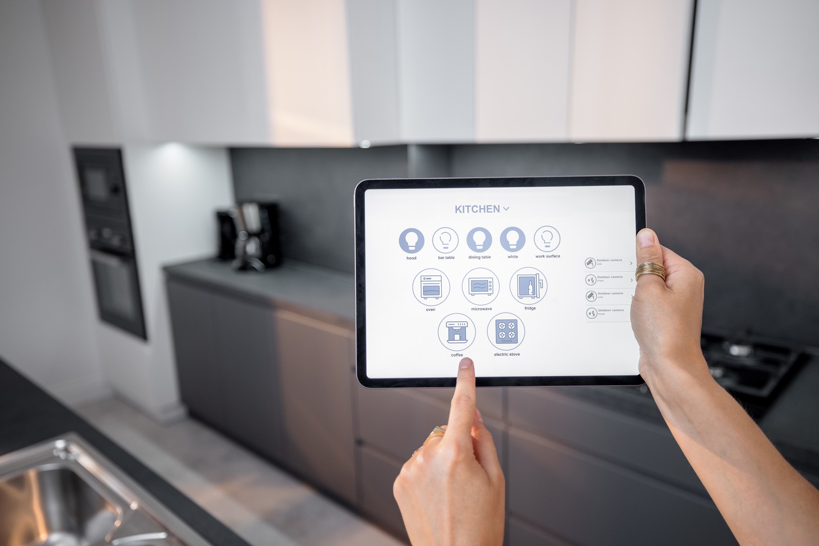 Digital tablet with running mobile application to control smart devices in the kitchen. Female controlling smart devices remotely at home. Smart home concept